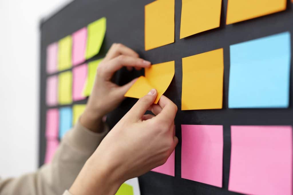 Πλάγια όψη χεριών που κολλάνε ένα κίτρινο post-it, υποδεικνύοντας την οργάνωση και την κατηγοριοποίηση περιεχομένου σε blog.