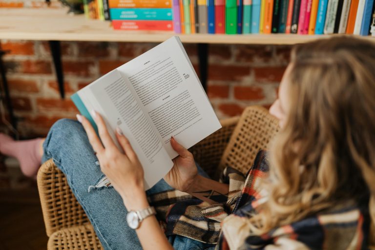 Γυναίκα που διαβάζει βιβλίο αυτοβελτίωσης σε ήρεμο και ζεστό χώρο, σύμβολο προσωπικής ανάπτυξης και αυτογνωσίας.